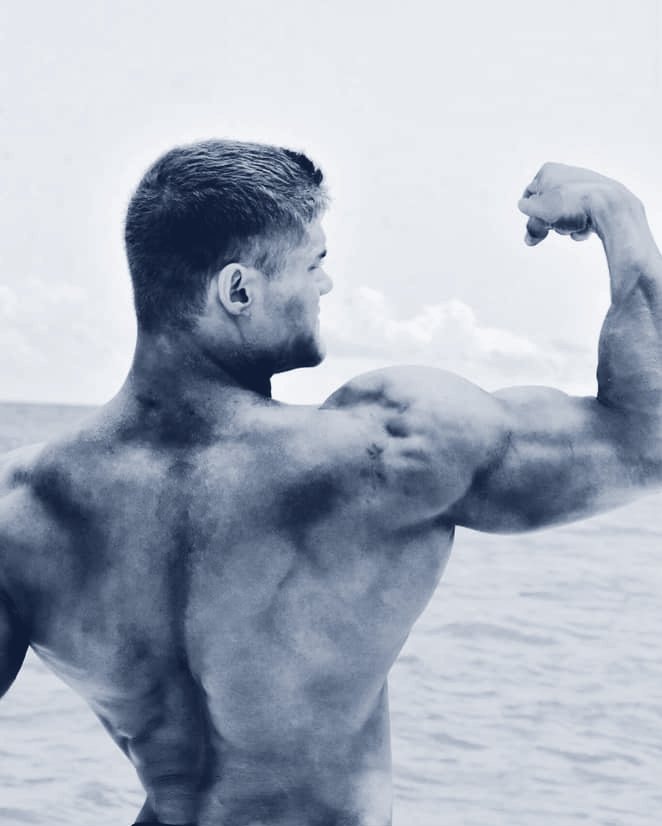 Benjamin Jones, seen from behind, flexing his right arm beside the water.