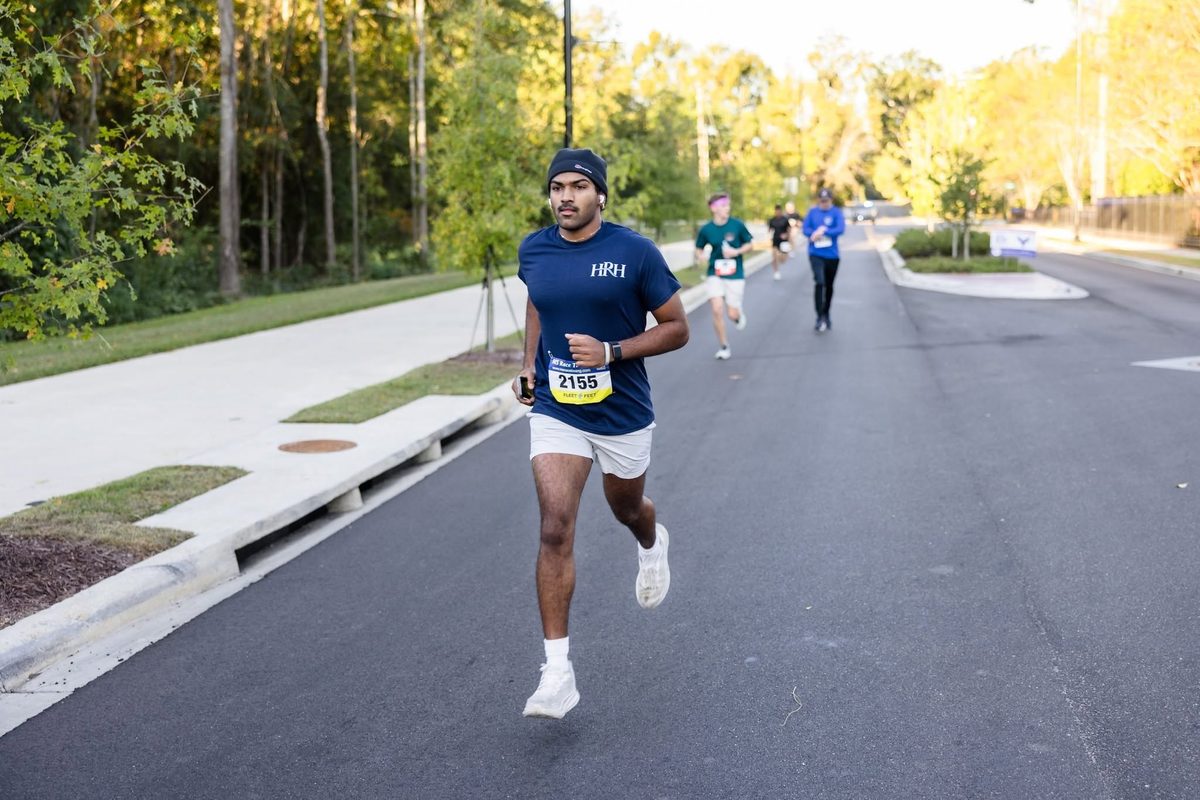A runner in a navy HRH shirt alone on the course, with the road curving away behind him.