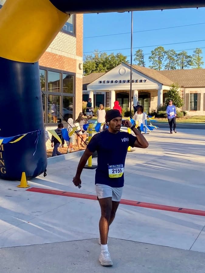 A runner in a navy HRH shirt coming through the inflatable finish arch.