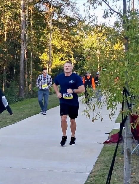 A runner in a navy HRH shirt and black shorts coming down the sidewalk toward the finish.