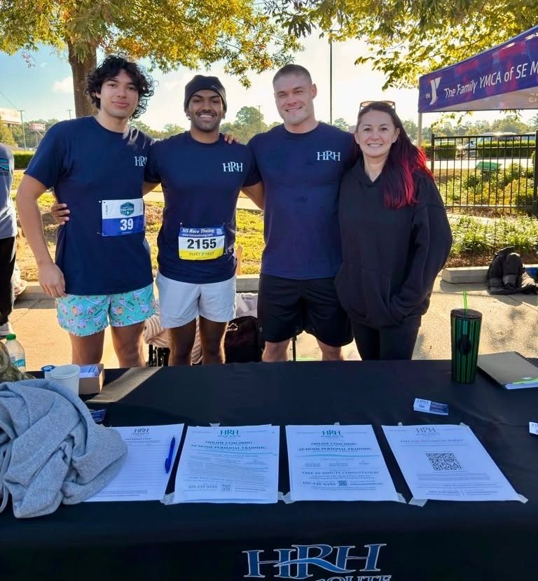 Four members of the Home Route Health crew in navy HRH shirts, standing behind the HRH table after the race.